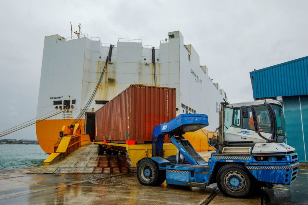 A PORT VEHICLE PULLS A CONTAINER FROM THE OPEN HATCH OF A CONTAINER VESSEL IN THE RAIN