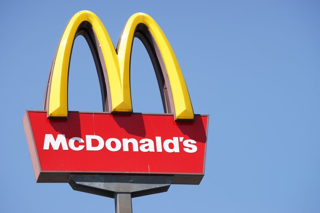 A large yellow 'M' on a signpost, above "McDonald's" written in white lettering on a red background.