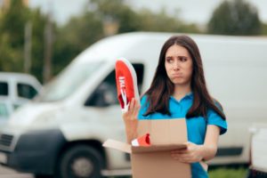 A YOUNG WOMAN HOLDS A RED SNEAKER ABOVE AN OPEN BOX, A LOOK OF DISAPPOINTMENT ON HER FACE