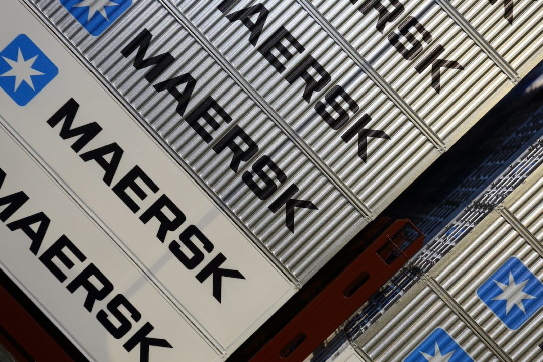 A view from above of rows of grey shipping containers with "MAERSK" written in large black letters on each one, next to a blue star logo