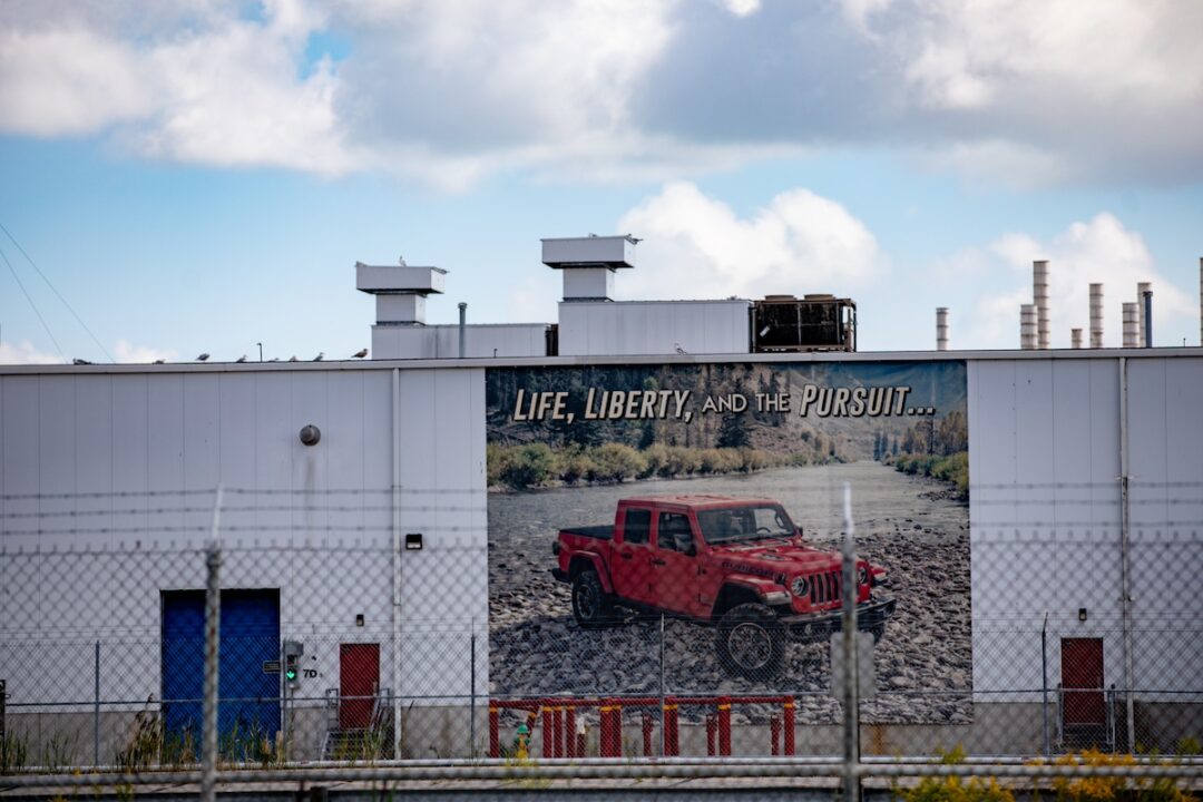 A large white factory building, with a large banner bearing an image of a red Jeep over the front.  