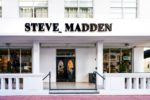 AN ELEGANT WHITE STOREFRONT BEARS THE WORDS STEVE MADDEN IN BLACK ABOVE THE DOOR