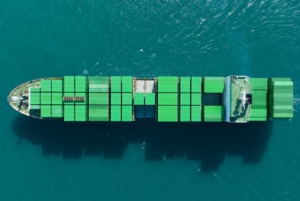 An overhead view of a cargo ship, with rows or green shipping containers stacked on the surface