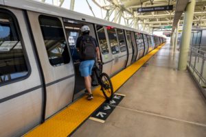 A PERSON IN BLUE SHORTS PUSHES A BICYCLE ON BOARD A LIGHT RAIL CAR