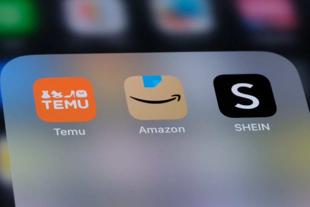 An app screen of a phone, depicting an orange icon with white writing that reads "Temu," a brown icon with an arrow shaped like a smile for Amazon, and a black icon with a white "S" representing Shein.