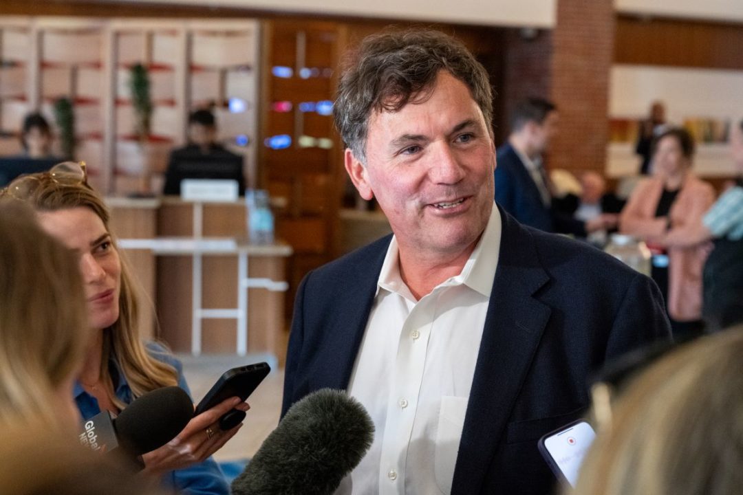 A MAN IN A JACKET AND WHITE SHIRT IS INTERVIEWED BY REPORTERS