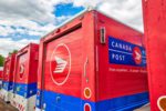 A row of red, blue and white striped mail trucks, with "Canada Post" written in white lettering on a blue square across the side of each vehicle