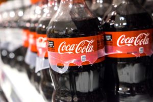 DOZENS OF PLASTIC BOTTLES WITH COCA-COLA LABELS SIT ON A SHELF