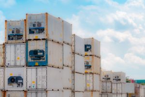 Stacks of white shipping containers, with blue machinery protruding from the front row of containers