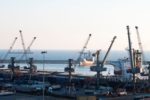 A CARGO SHIP SITS IN THE HARBOR OF A SMALL PORT WITH CRANES