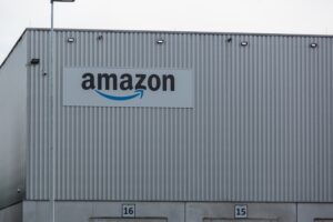 A metal grey warehouse building, with "Amazon" written in black lettering across the top left