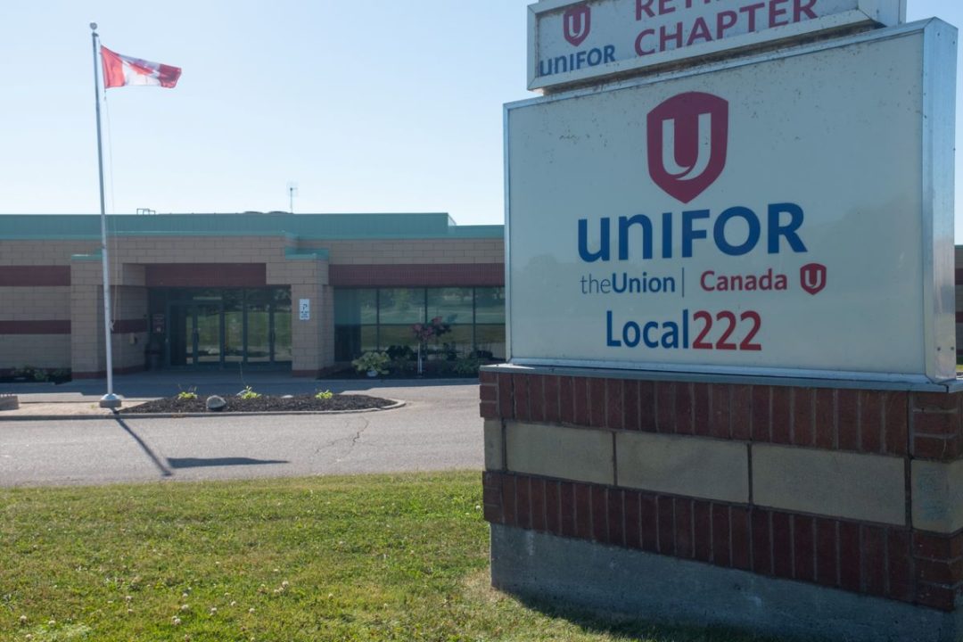 A CANADIAN FLAG AND SIGN BEARING THE WORDS UNIFOR UNION CANADA SIT OUTSIDE AN OFFICE COMPLEX