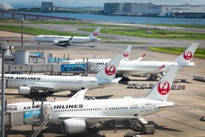 SEVERAL AIRPLANES BEARING THE JAPAN AIRLINES LOG SIT ON THE TARMAC OF AN AIRPORT.