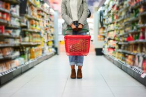 Supermarket aisle, woman legs and basket for shopping in grocery store. 