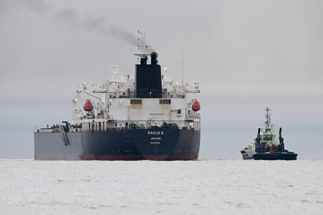 A black and white oil tanker with a black smokestack, next to a smaller black ship in the open sea