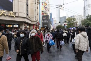 A BUSY STREET IN CHINA WITH MANY PEOPLE WEARING MASKS