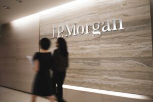 TWO WORKERS, SEEN BLURRILY IN MOTION, WALK PAST A GIANT MARBLE WALL BEARING THE LETTERS JPMORGAN