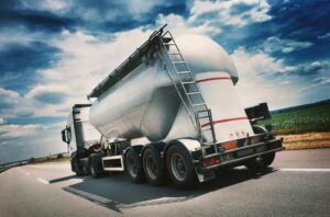 A SHINY SILVER FUEL OIL DELIVERY TRUCK DRIVES DOWN A HIGHWAY