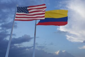 The U.S. and Colombian flags flying next to each other on flag poles against a cloudy sky