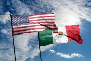 AMERICAN AND MEXICAN FLAGS FLUTTER AGAINST A CLOUD-STREAKED BLUE SKY