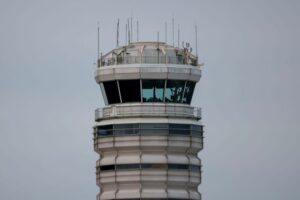 AN AIR TRAFFIC CONTROL TOWER IS SILHOUETTED AGAINST A GREY SKY