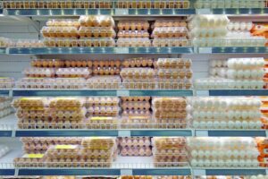 Five shelves in a grocery store dairy aisle filled with cartons of brown and white eggs