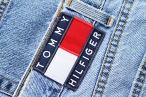 A close up of a pair of blue jeans, with a red and white patch that reads "Tommy Hilfiger" over the top and bottom of the square