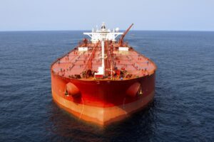 A large orange oil tanker ship seen from the front, moving through the open sea on a clear day