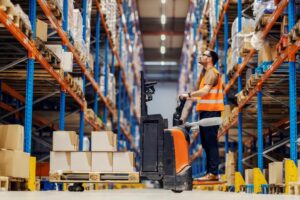 A WORKER OPERATES A FORKLIFT IN THE AISLE OF A WAREHOUSE356.jpg