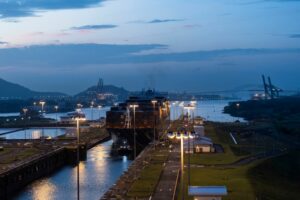 A SHIP PASSES THROUGH A CANAL LOCK AT NIGHT, LIGHTS GLEAMING ALL AROUND.