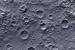 An overhead view of the surface of the moon, covered in grey dust and craters.