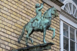 An oxidised bronze sign of a post boy or man on horseback attached to the wall of a building.